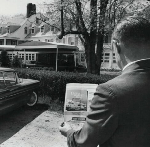 Historic image of man looking at Canoe Place with vintage advertisement in hand.