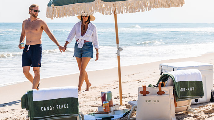 couple walking the beach with Canoe Place towel and bag and umbrella