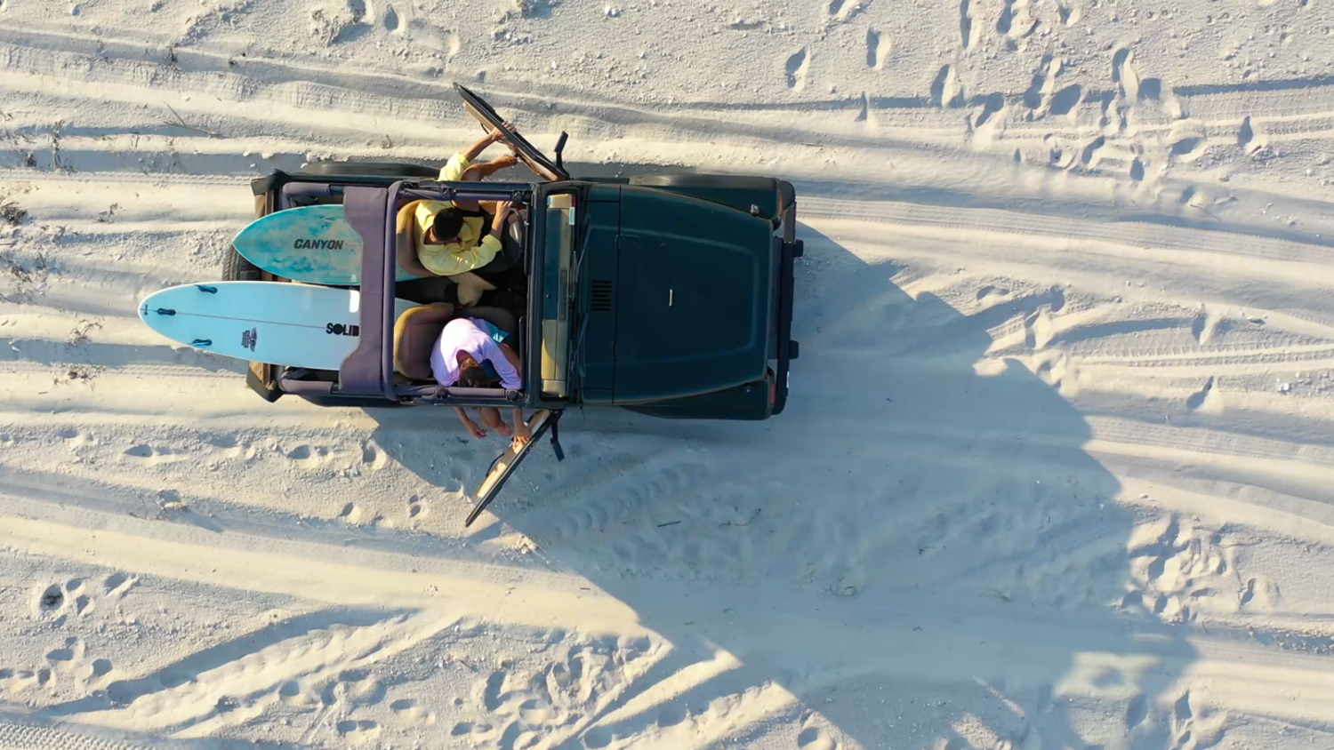 People driving jeep on a beach with surfboards