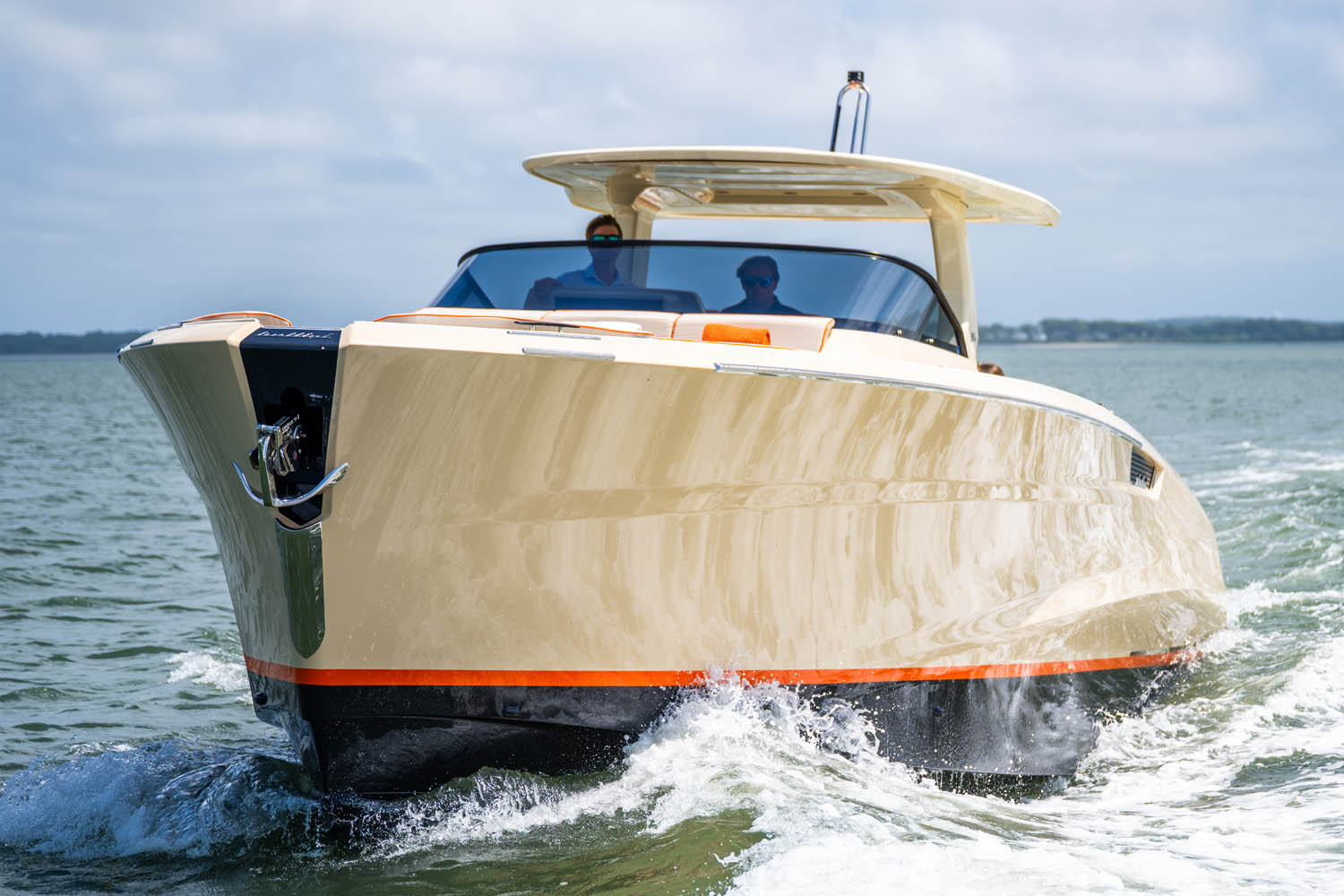 Front bow view of a cream and orange luxury yacht cutting through choppy water on a sunny day.