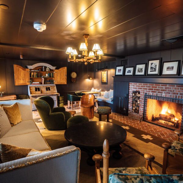 Cozy fireplace lounge with a round coffee table, dark paneled walls, and framed photographs above the mantel.